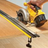 The Rockler 52'' to 104'' Low Profile Straight Edge Clamp System assisting a saw in cutting a board