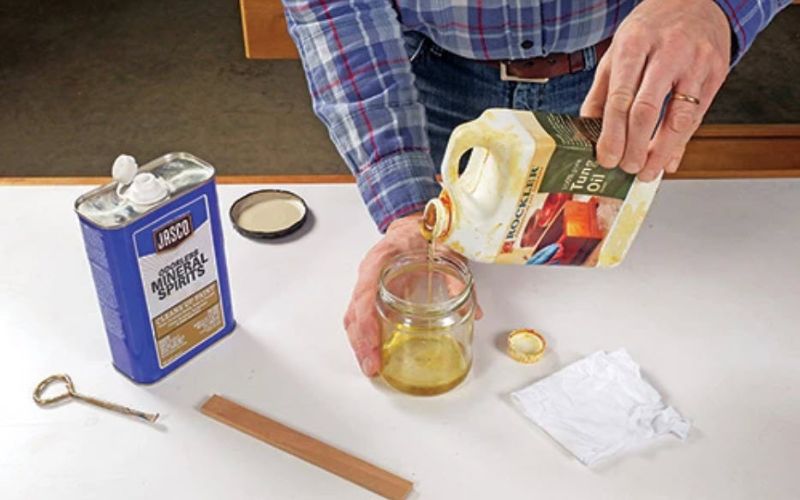 man pouring tung oil into glass container