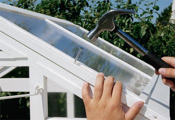 Hammering bolts into place on fold-up greenhouse roof