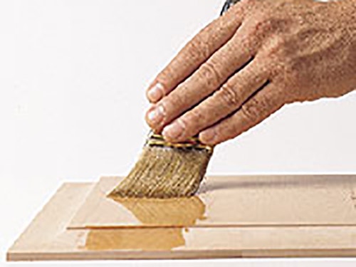 Wiping coat of clear finish over cabinet panel with brush