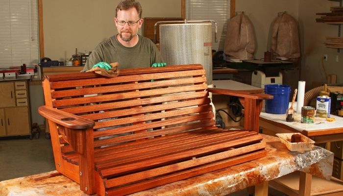 man finishing porch swing with wood stain
