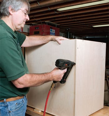 Using staple gun to apply kitchen cabinet backing