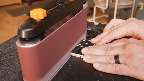 Using a benchtop belt sander to finish smoothing out the domino edges