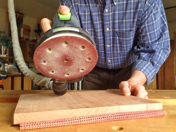 Applying a random orbit sander to a piece of lumber